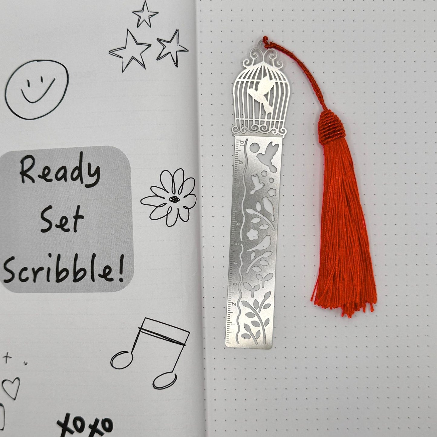 Metal bookmark with red tassel on a notebook page with doodles
