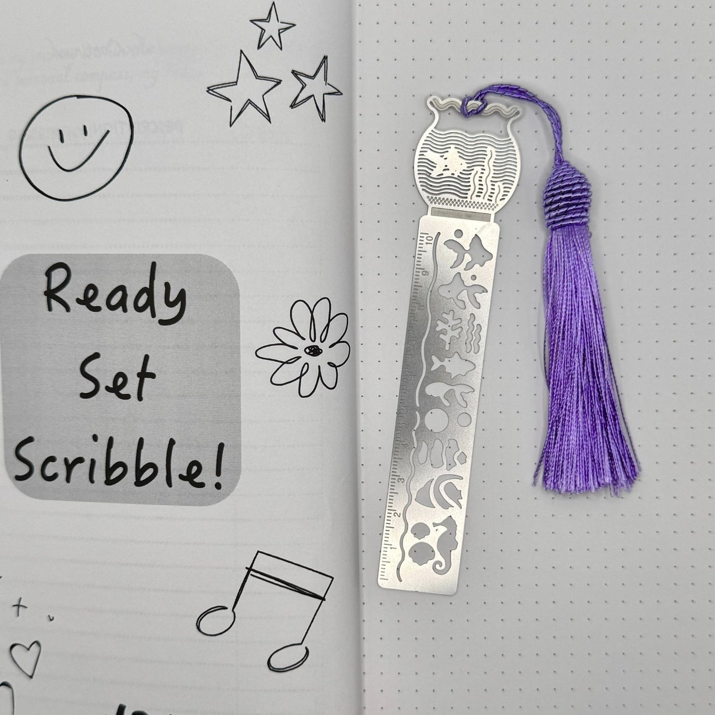 Metal bookmark with purple tassel on a gray background with doodles