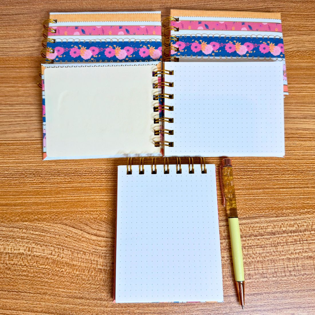Small spiral-bound dotted notebooks with floral design on a wooden surface