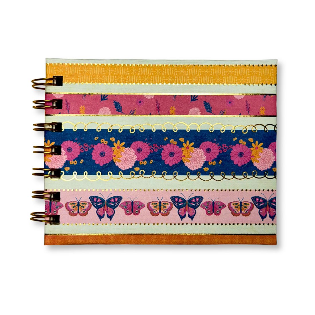 Top-down view of a handmade Love To Scribble mini notebook featuring colorful horizontal bands of pink florals, butterflies, and gold foil accents.