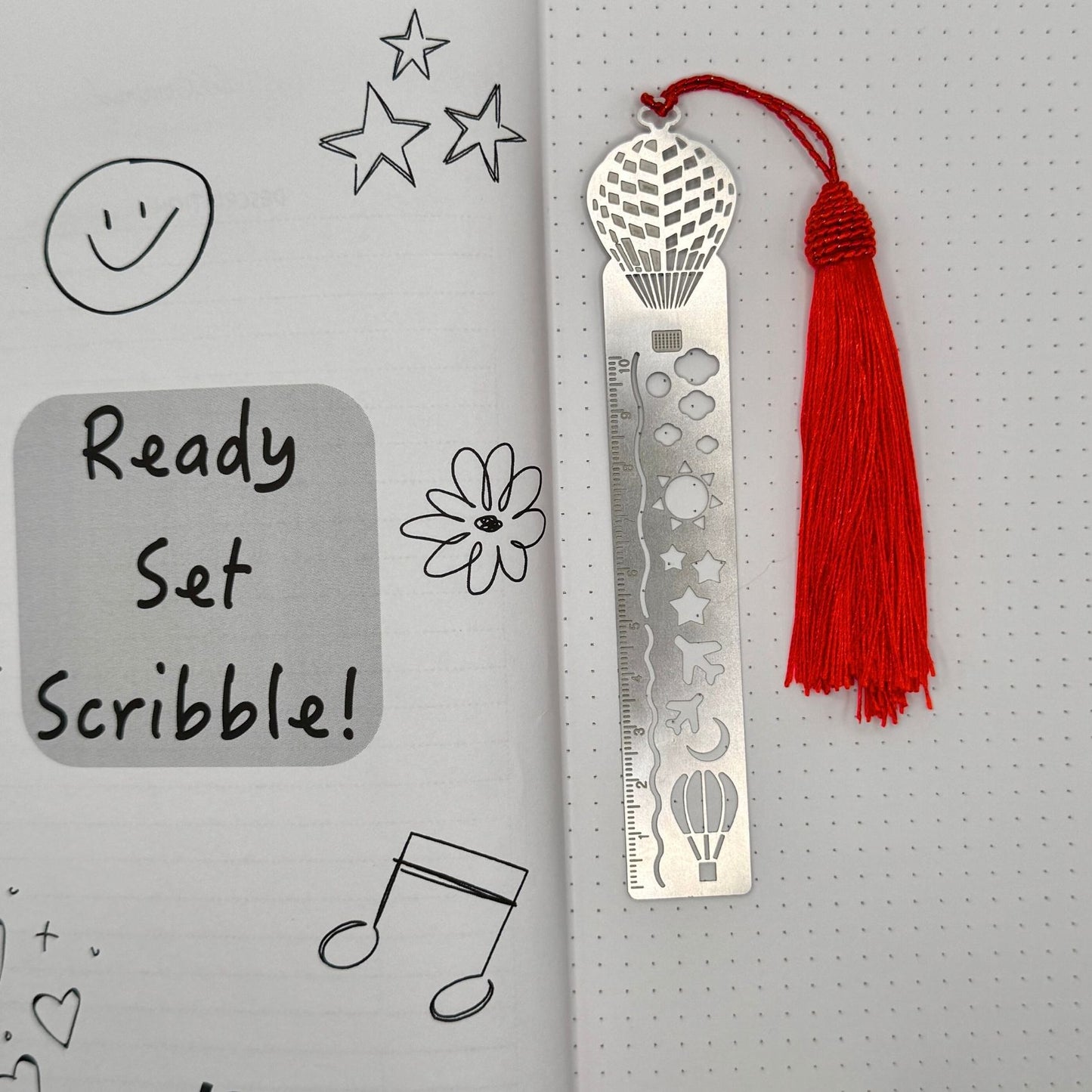 Metal bookmark with red tassel on a gray background with doodles