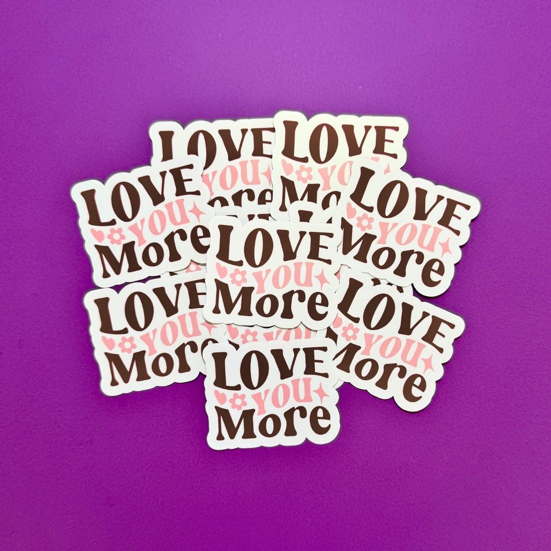 Stack of 'I LOVE YOU MORE' stickers on a purple background