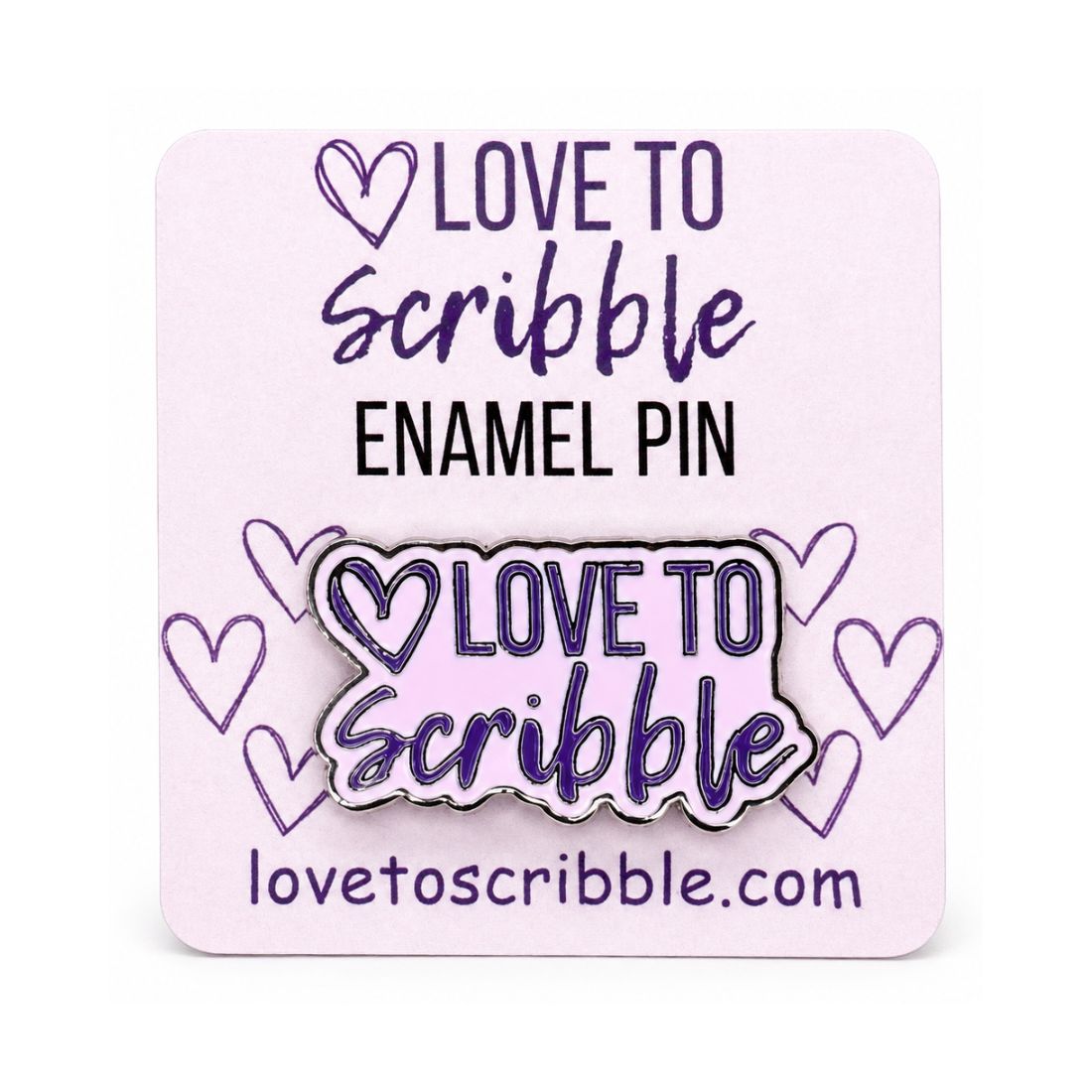 A square pink display card holding an enamel pin that reads “LOVE TO Scribble” with purple hearts and the website lovetoscribble.com.