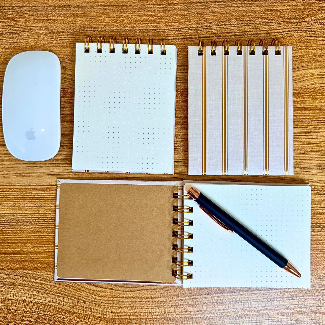 Size comparison of the gold stripe mini notebook next to a white computer mouse and a black pen on a wooden desk.