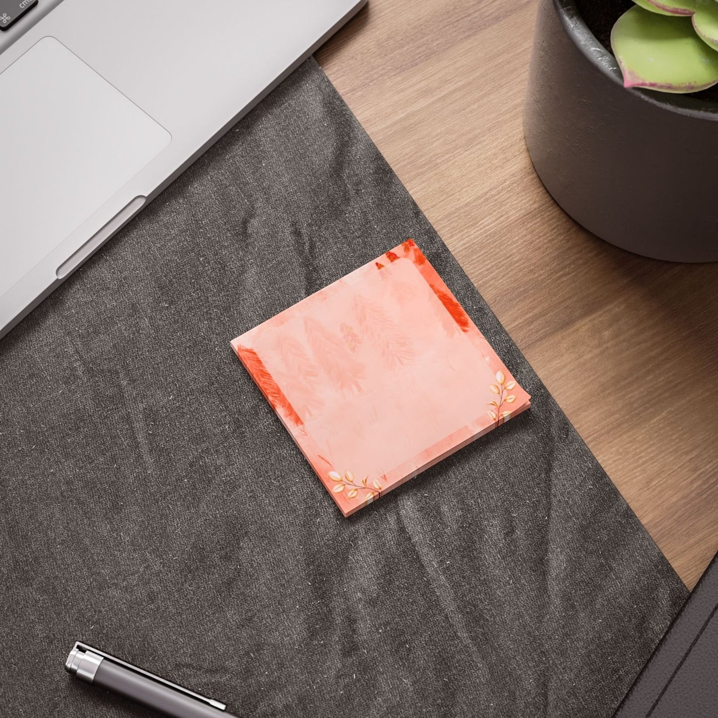 Orange square sticky notes on a gray textured surface with a laptop and plant in the background