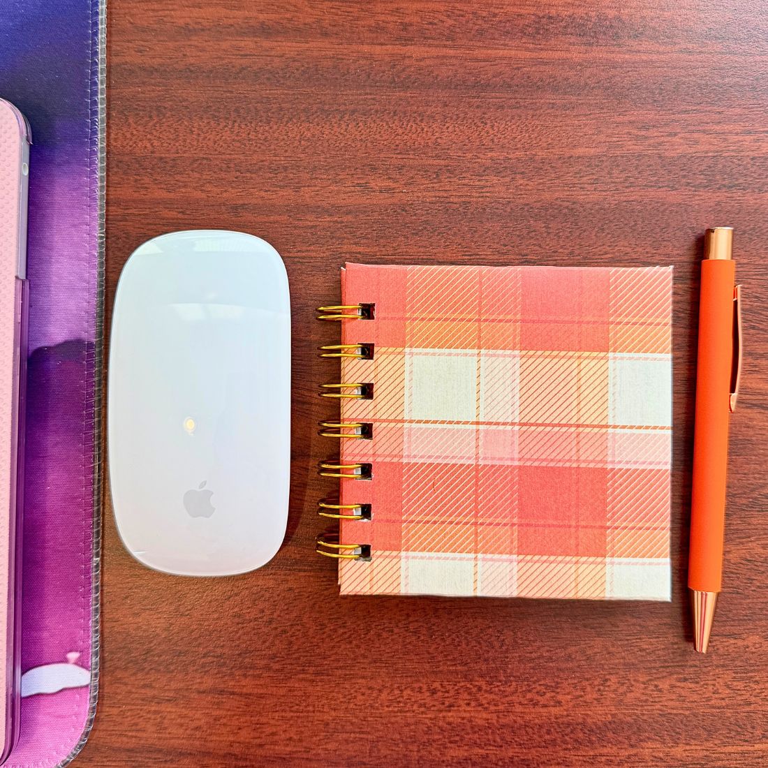 Plaid notebook, white mouse, and orange pen on a wooden desk