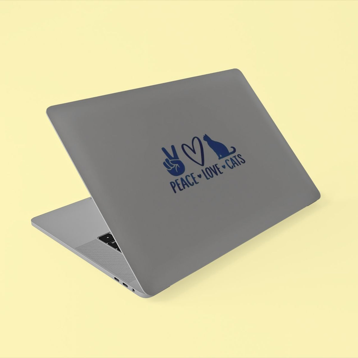 A silver laptop with a dark blue graphic on the lid showing a peace hand sign, a heart, a cat silhouette, and the text 'PEACE LOVE CATS', set against a pale yellow background.