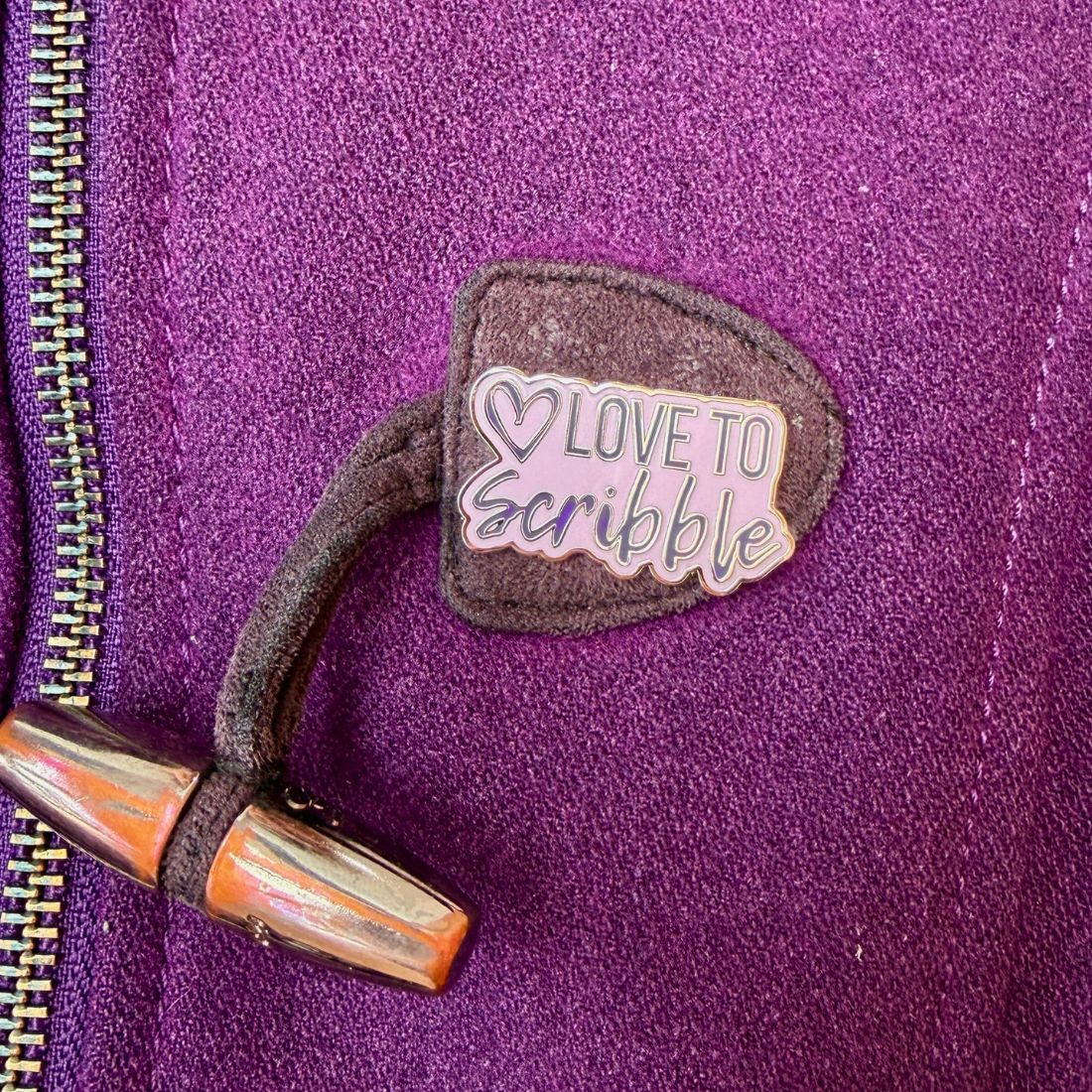 Enamel Pin with 'Love to Scribble' text on a purple jacket